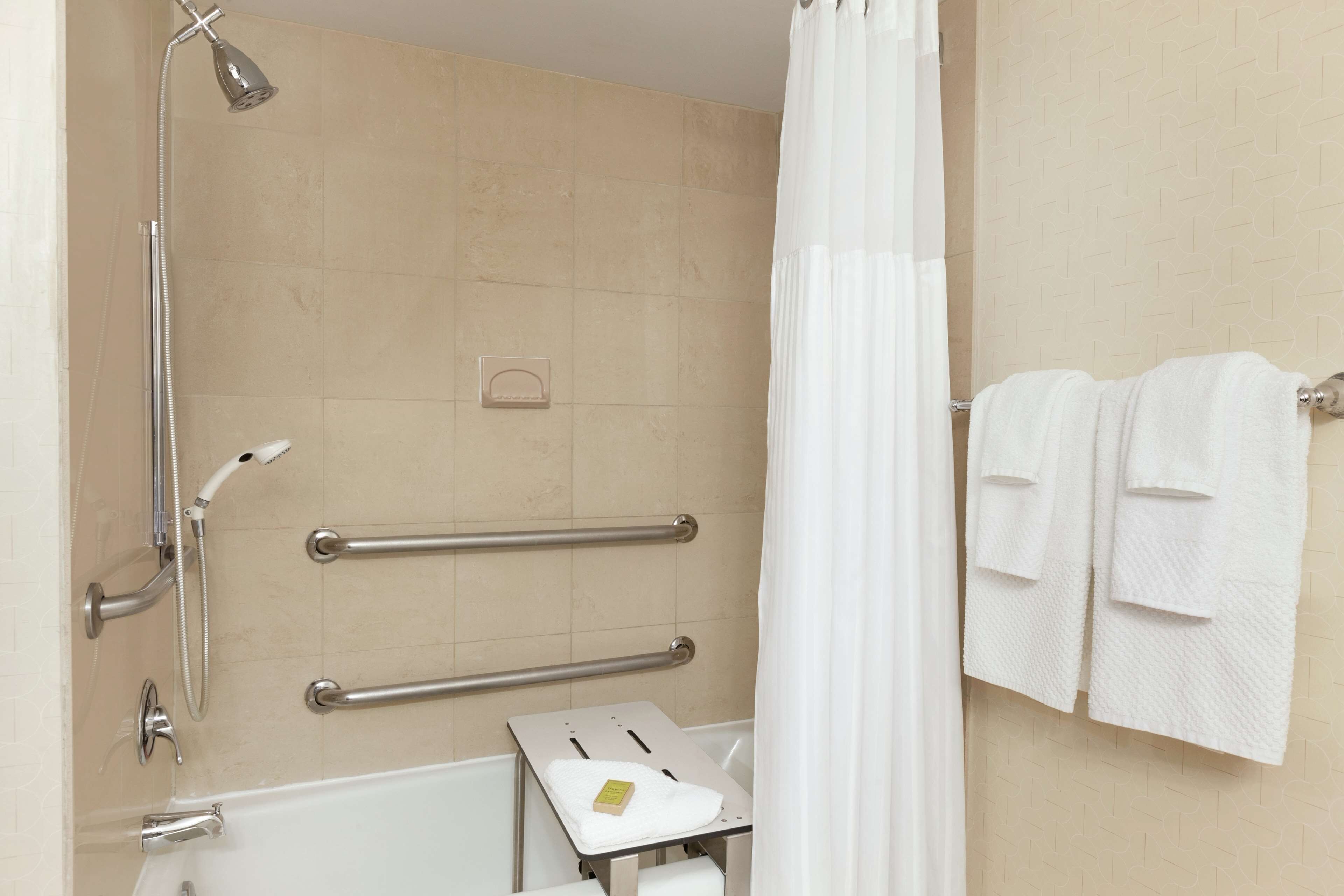 Baño con ducha, barras de apoyo, toallero y portarrollo de papel higiénico.
