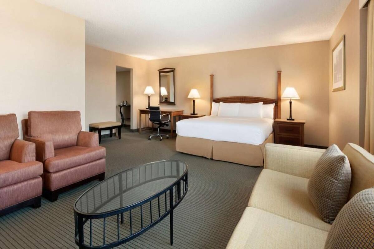 A hotel room with a bed, two armchairs, a sofa, a desk with a chair, a mirror, and two bedside lamps.