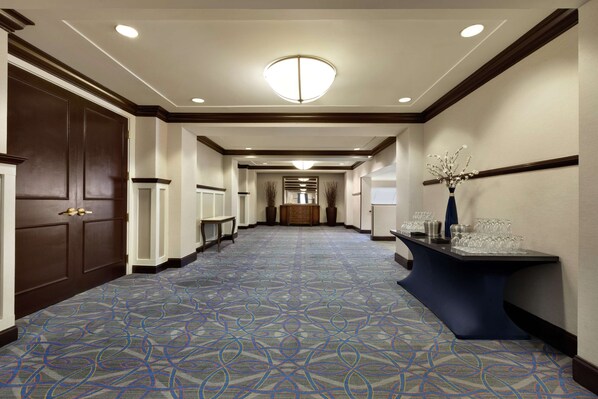 A hotel corridor with patterned carpet, wooden doors, a reception desk, and a decorative vase. - DoubleTree by Hilton Hotel Annapolis (Annapolis)