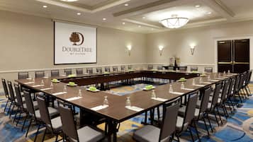A conference room with a long table, chairs, and a projector screen displaying "DOUBLETREE by Hilton".