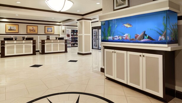 A hotel lobby with a reception desk, a large aquarium, and framed artwork on the walls.