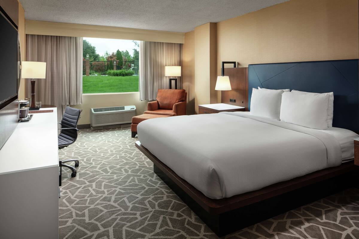 A hotel room with a large bed, a desk, a chair, and a TV.