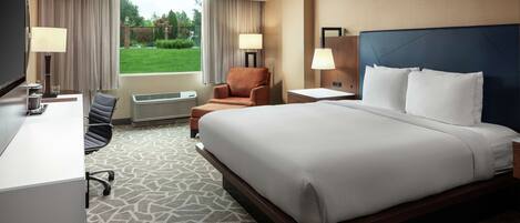 A hotel room with a large bed, a desk, a chair, and a TV.
