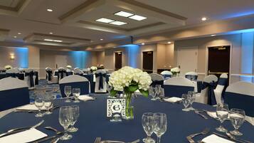 A banquet hall with round tables set for a formal event, each with place settings, glasses, and a centerpiece.
