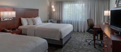A hotel room with two beds, a desk with a TV, a chair, and a lamp.