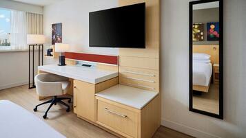 A hotel room with a bed, a desk with a chair, a flat-screen TV, a lamp, and a mirror.