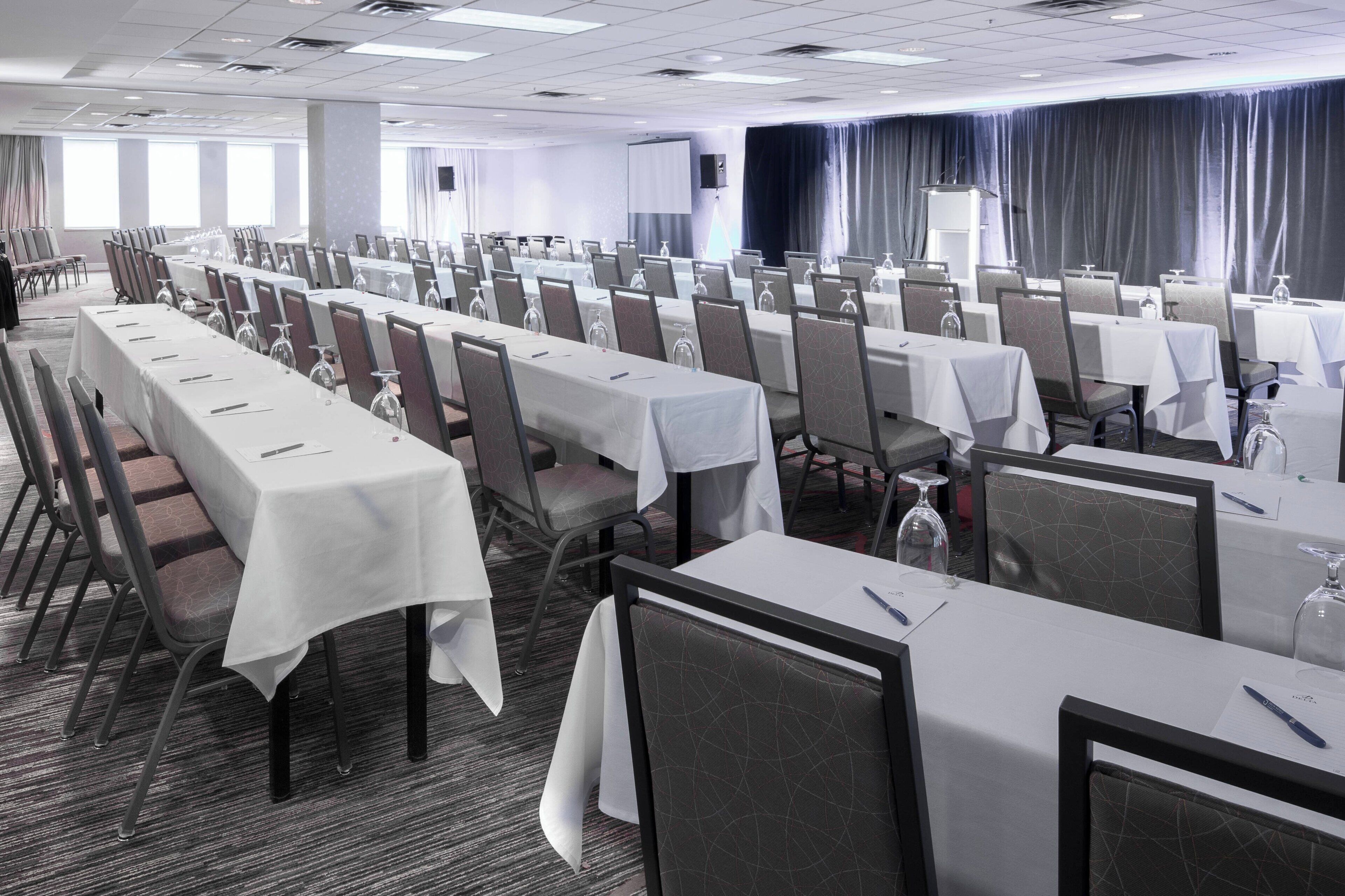 Un salón de conferencias con filas de mesas y sillas, equipado con botellas de agua y copas de vino.