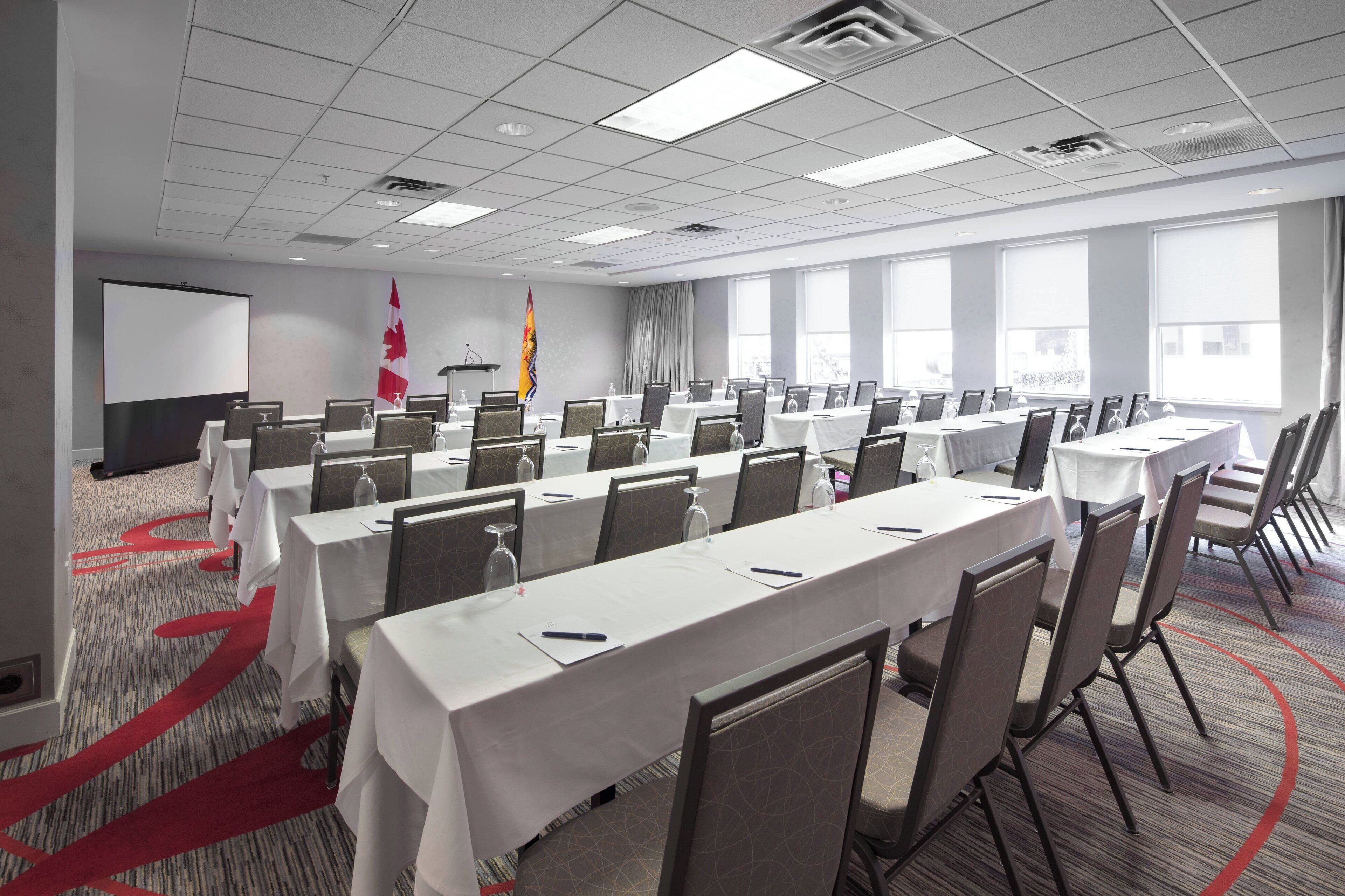 A conference room with multiple tables and chairs, a projector screen, and a Canadian flag.