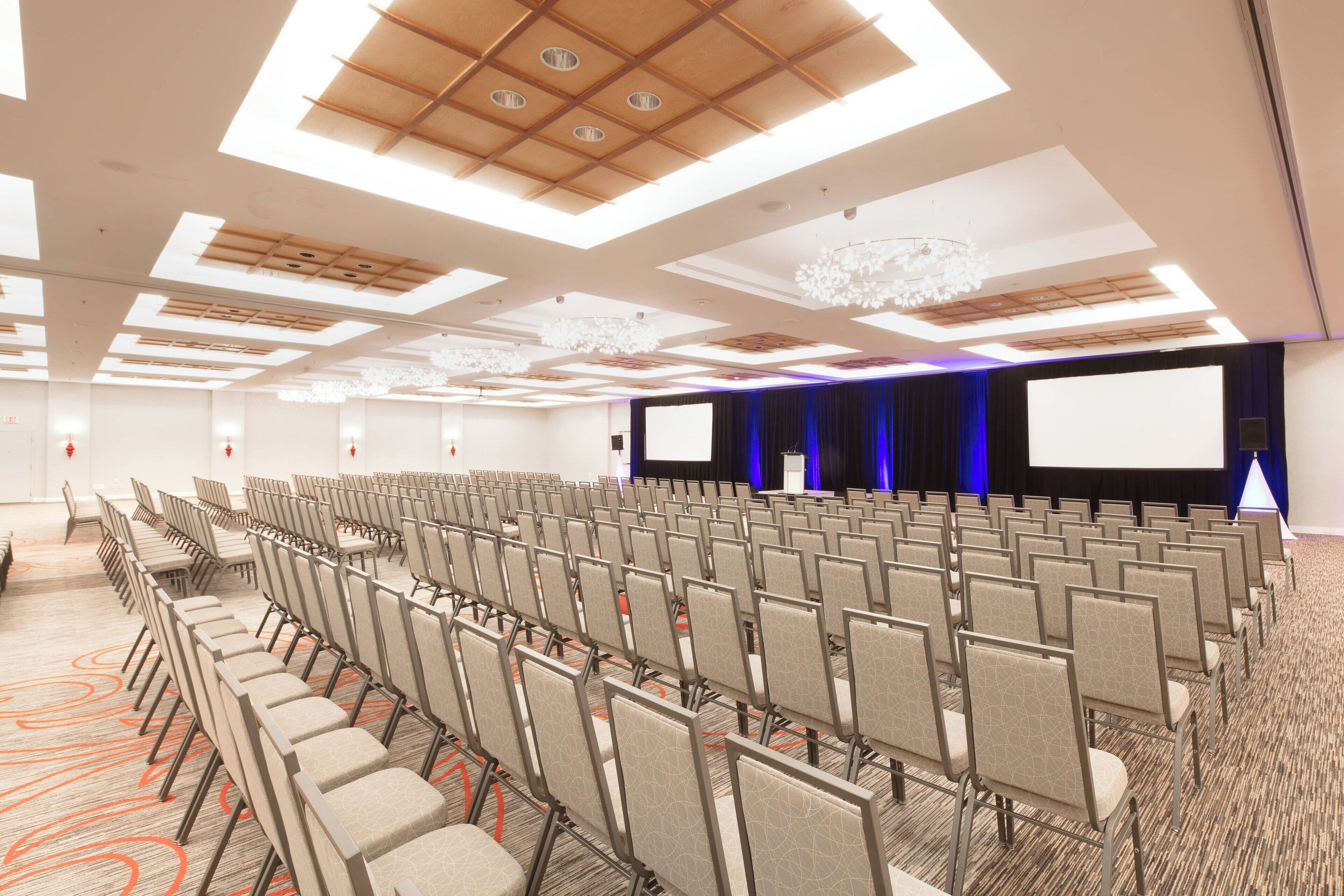Une salle de conférence avec des rangées de chaises, un grand écran et une scène équipée d’un pupitre.