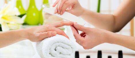 A close-up of hands receiving a manicure, with a towel and nail polish bottles in the background.