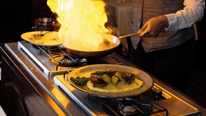 A chef performing a flambé with a pan on a stove.