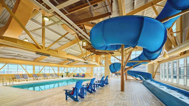 An indoor swimming pool with blue slides, lounge chairs, and a tiled floor.