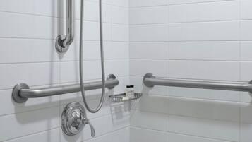 Zona de ducha con barra de apoyo, cabezal de ducha manual y desagüe en el suelo.