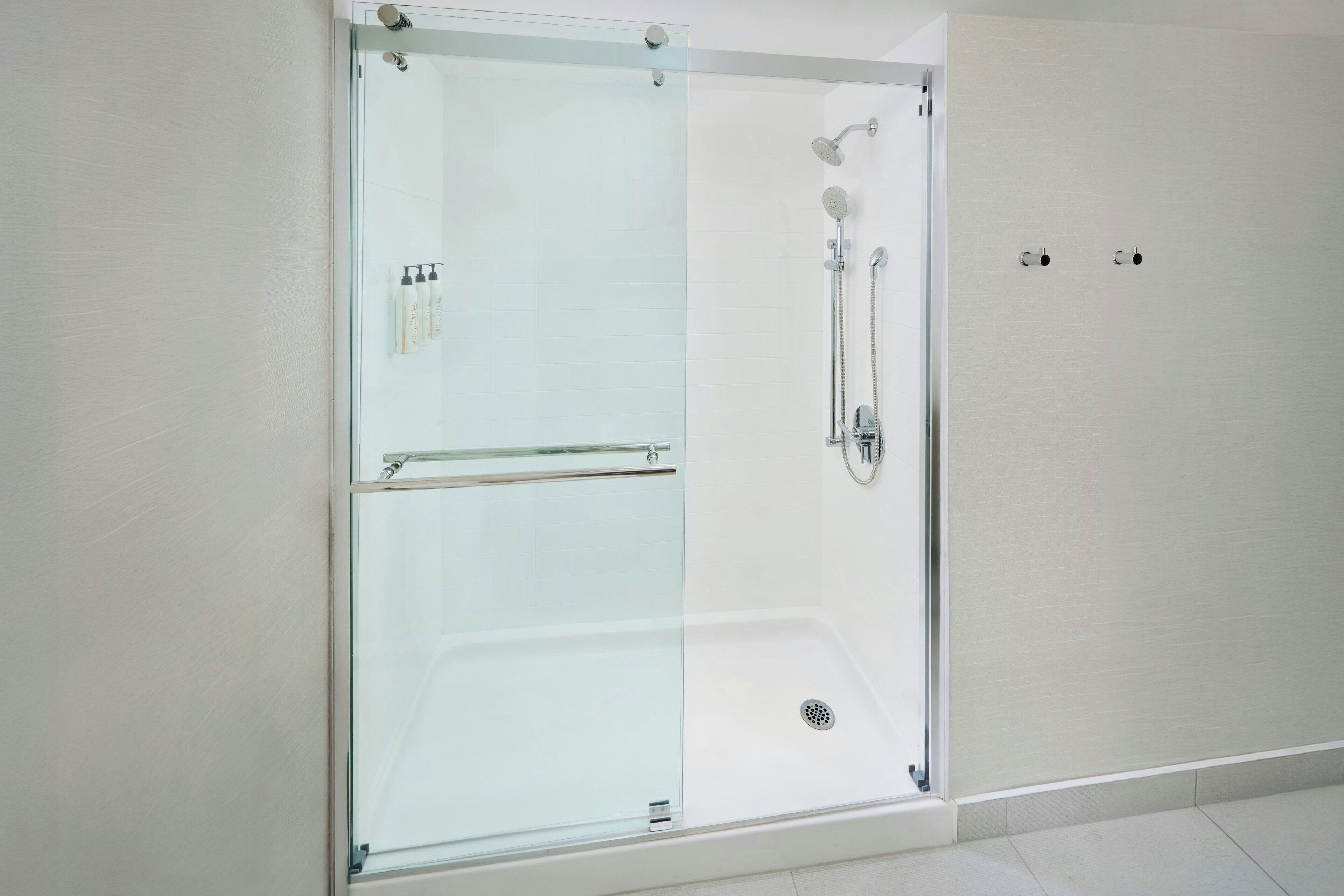 A modern bathroom with a glass-enclosed shower, a glass door, and a white tiled floor.
