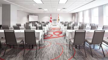 A conference room with rows of tables and chairs, a carpeted floor, and flags on the walls.