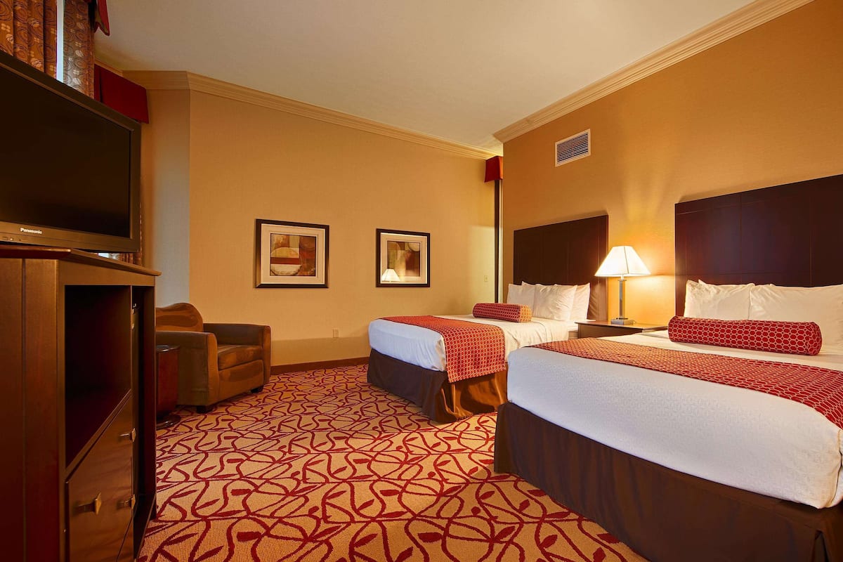 A hotel room with two beds, a TV, a desk, and a lamp.