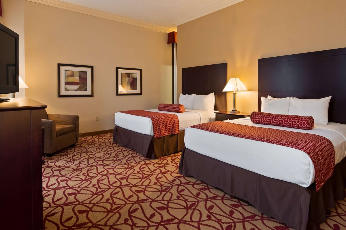 A hotel room with two beds, a TV, a desk, and a lamp.