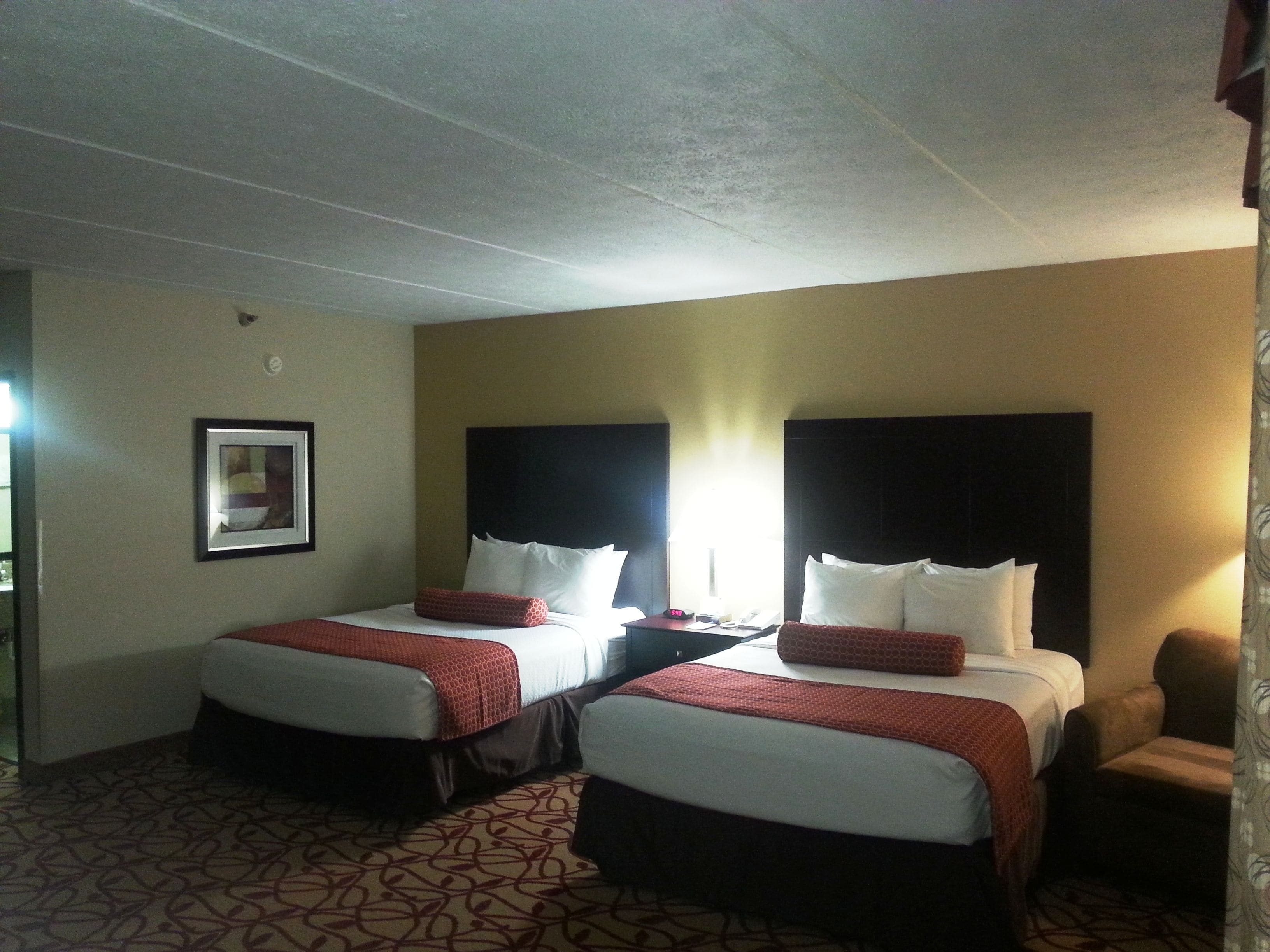 A hotel room with two beds, each with a red and white bedspread, a headboard, and a bedside table with a lamp.