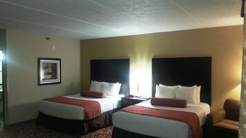 A hotel room with two beds, each with a red and white bedspread, a headboard, and a bedside table with a lamp.