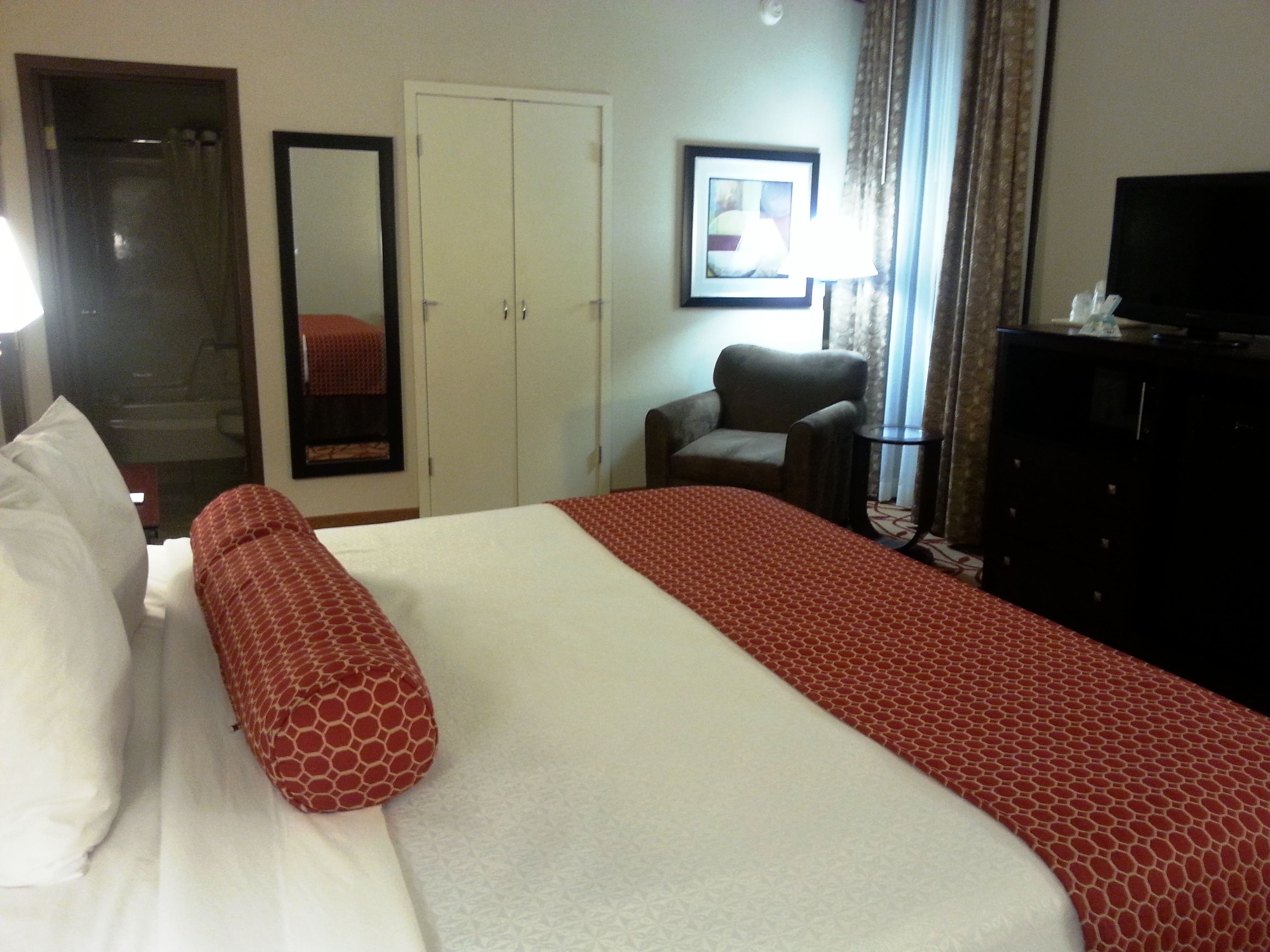 A hotel room with a bed, a wardrobe, a chair, a television, and a framed picture on the wall.
