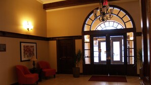 A lobby with a grand arched doorway, two red armchairs, a chandelier, and a framed picture on the wall. - Best Western Park Hotel (Warren)