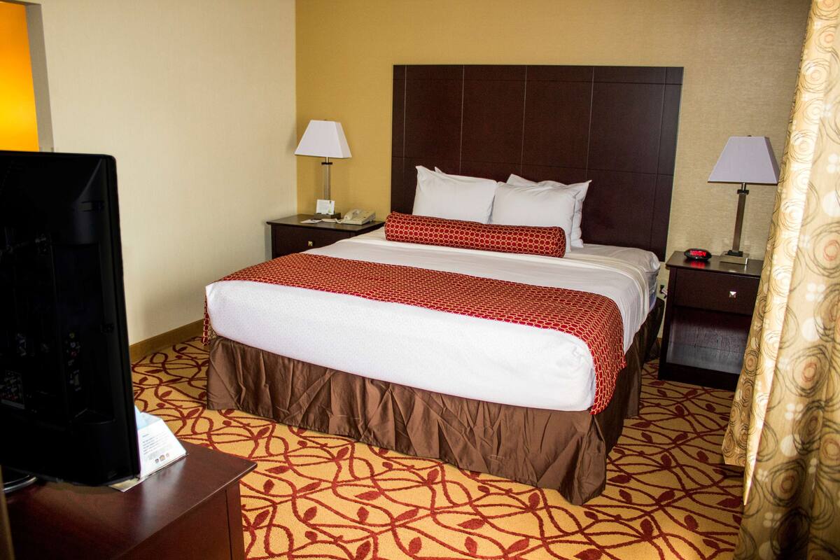 A hotel room with a large bed, two bedside tables with lamps, a TV on a stand, and patterned carpet.