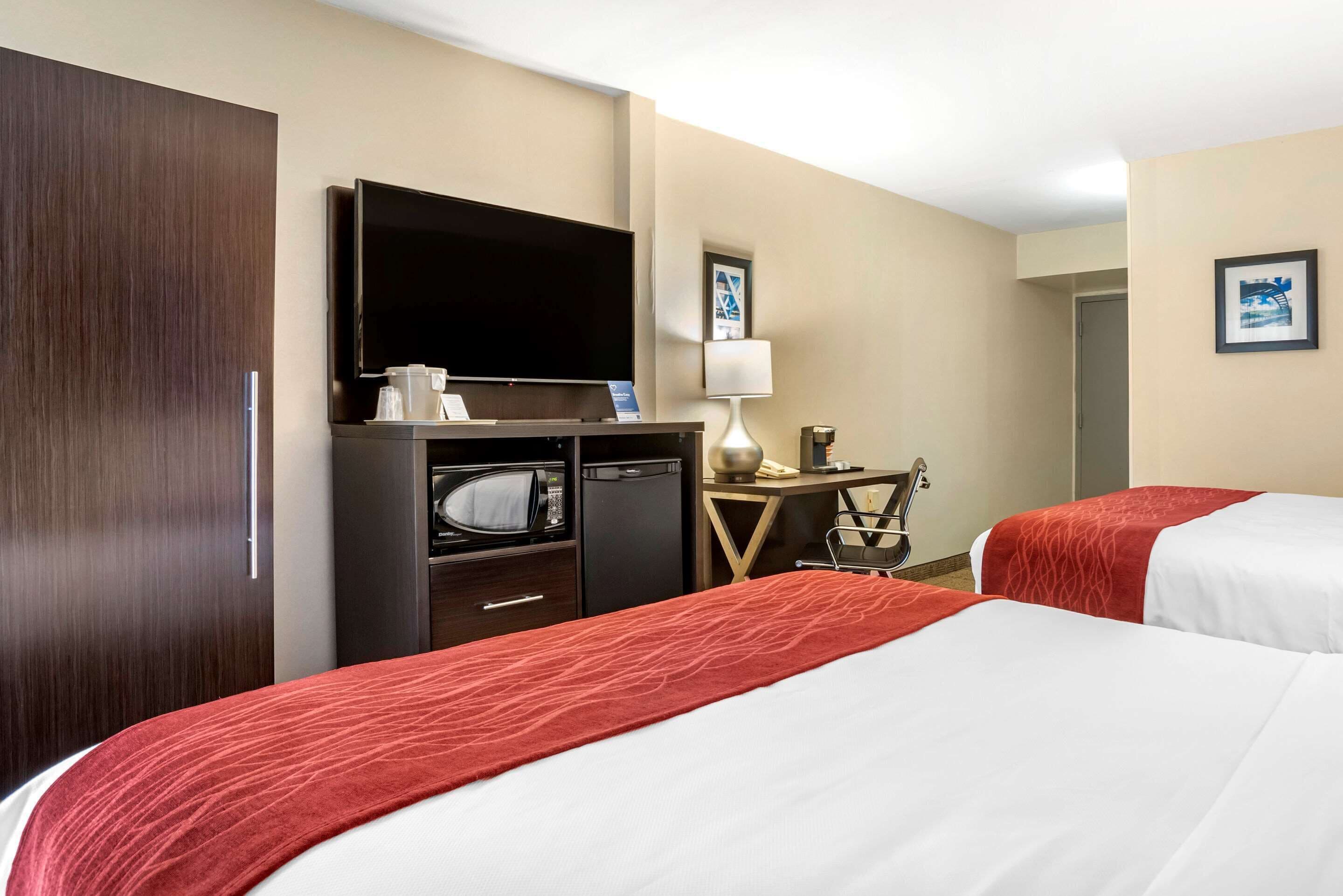 A hotel room with two beds, a TV, a desk with a lamp, and a microwave.