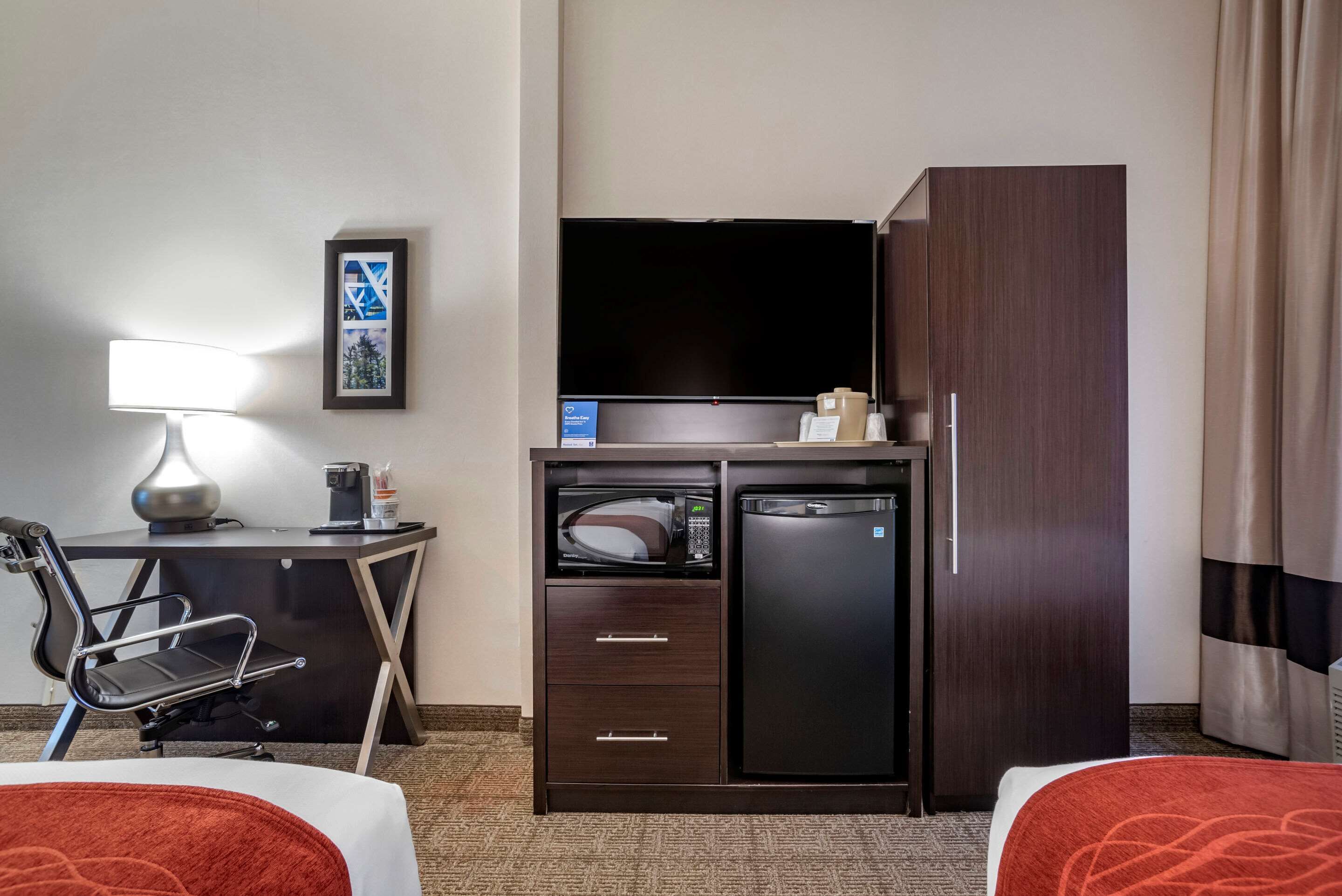 Habitación de hotel con cama, escritorio con lámpara, televisor, minibar y armario.