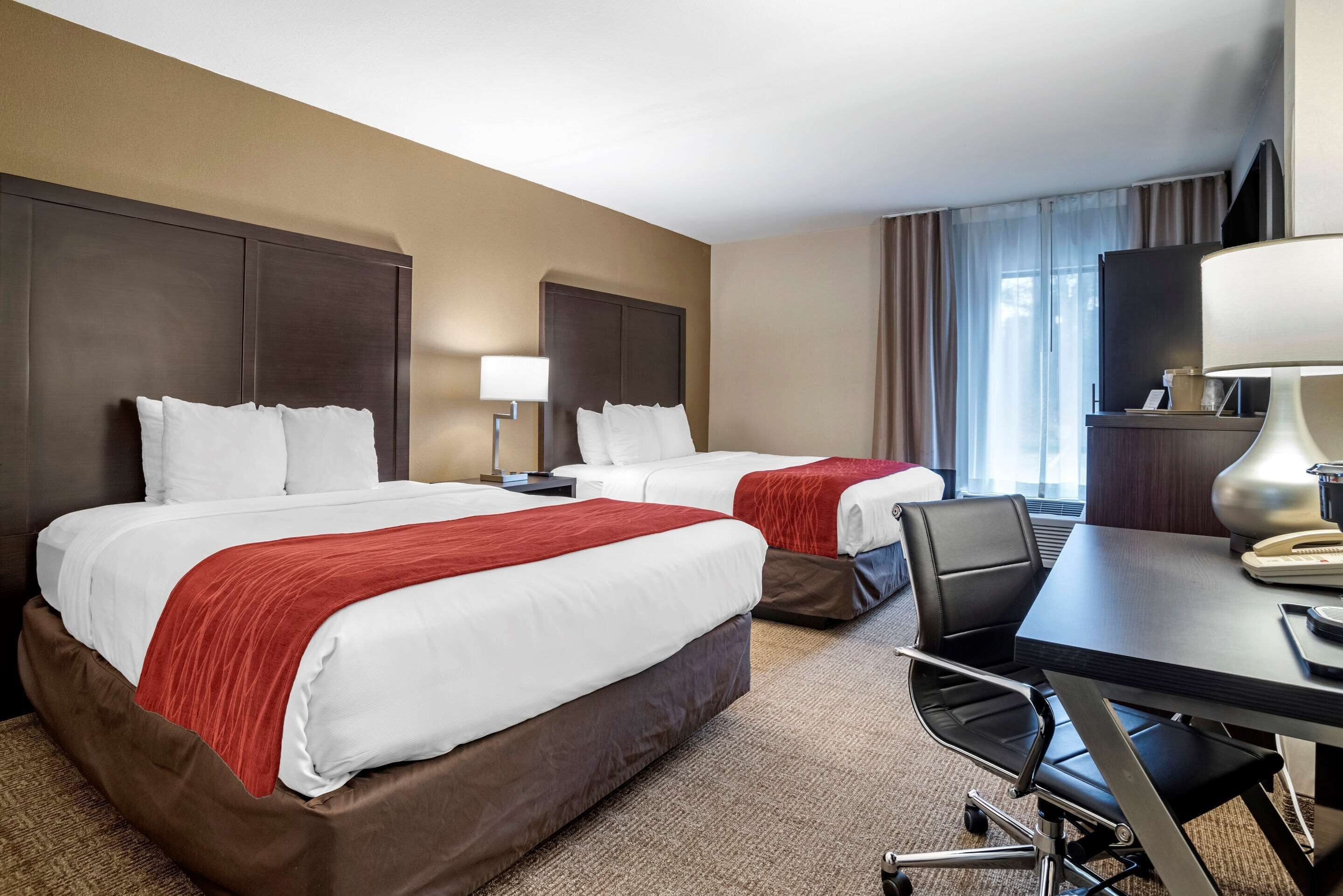 A hotel room with two beds, a desk, a chair, a lamp, and a television.