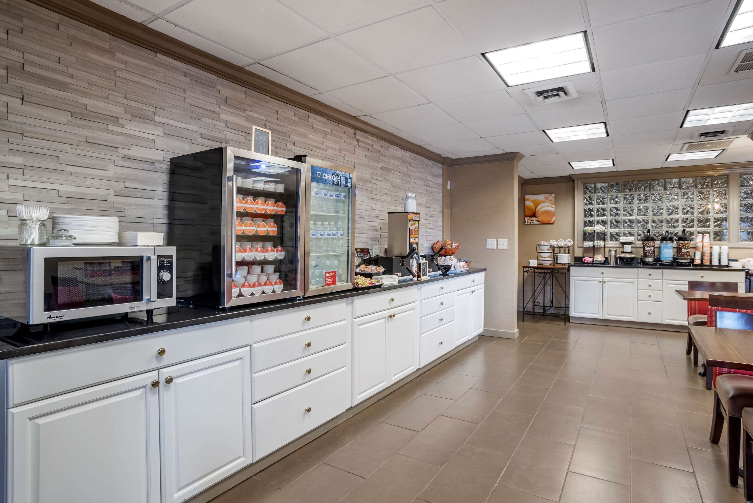 A modern kitchen with white cabinets, a microwave, a refrigerator, and a coffee station.