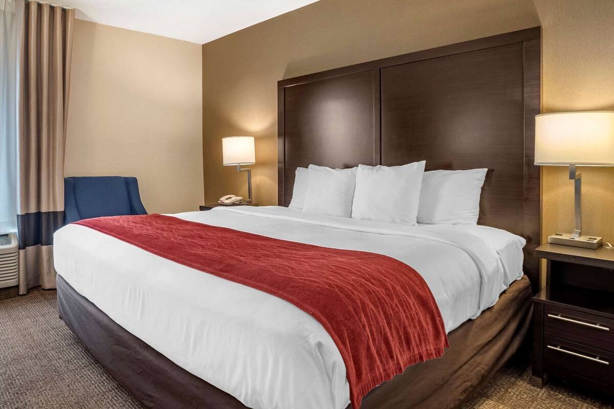 Habitación de hotel con una cama grande, una mesita de noche con lámpara, una silla y un teléfono.