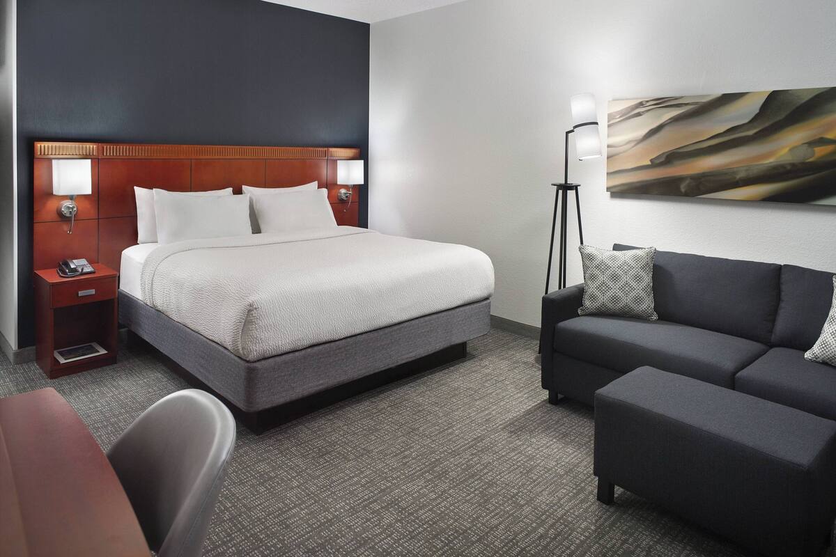 A hotel room with a large bed, a sofa, a desk, and a lamp.