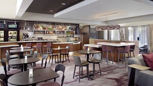 A modern hotel lobby with a bar area, multiple seating options including tables and chairs, and a large mirror. - Courtyard Charlotte Arrowood (Charlotte)