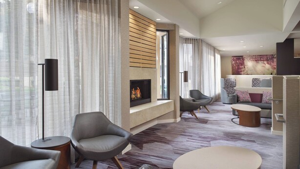A modern living room with a fireplace, comfortable seating, and a large window with sheer curtains. - Courtyard Charlotte Arrowood (Charlotte)