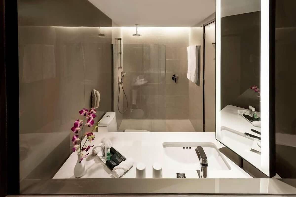 A modern bathroom with a glass-enclosed shower, a white sink with a mirror, and a vase of orchids.