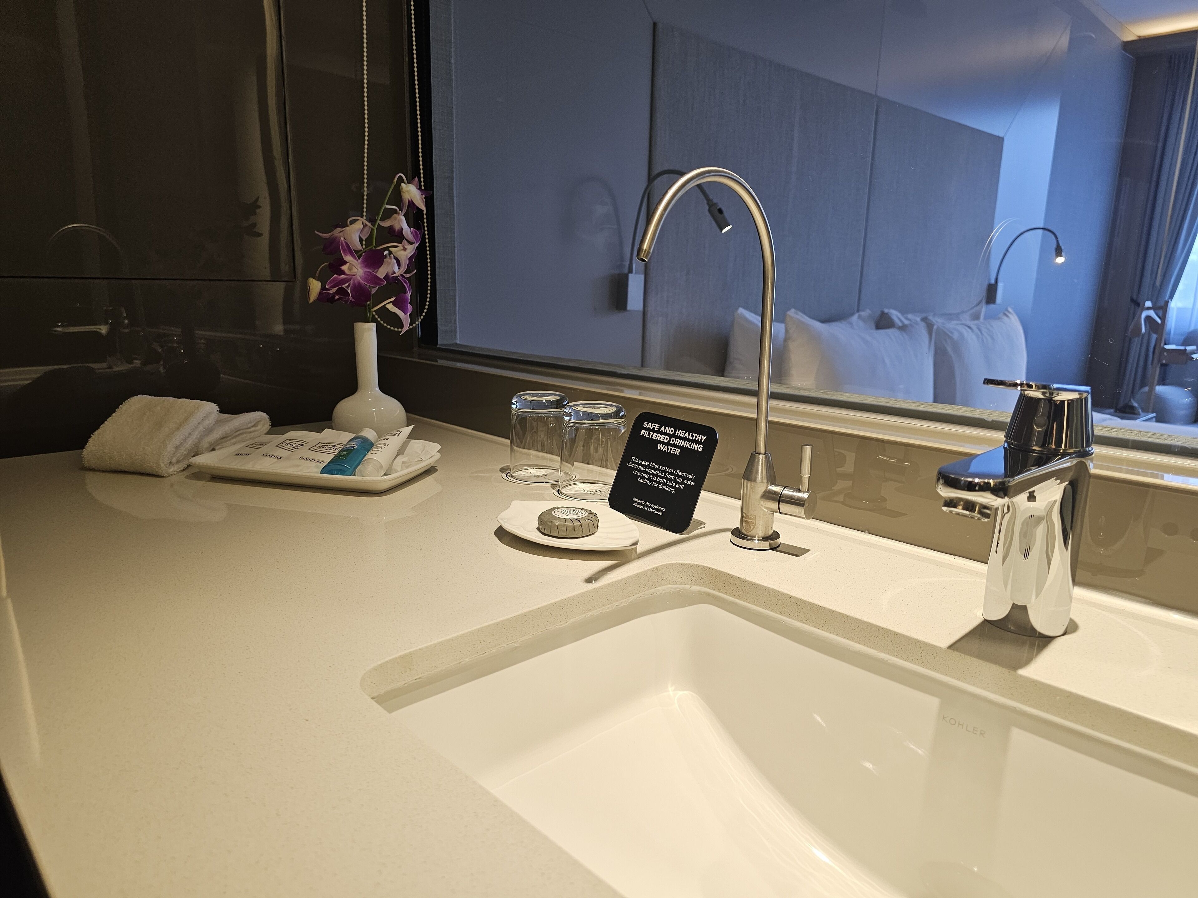A hotel bathroom with a sink, a mirror, a towel, toiletries, and a sign about water filtration.