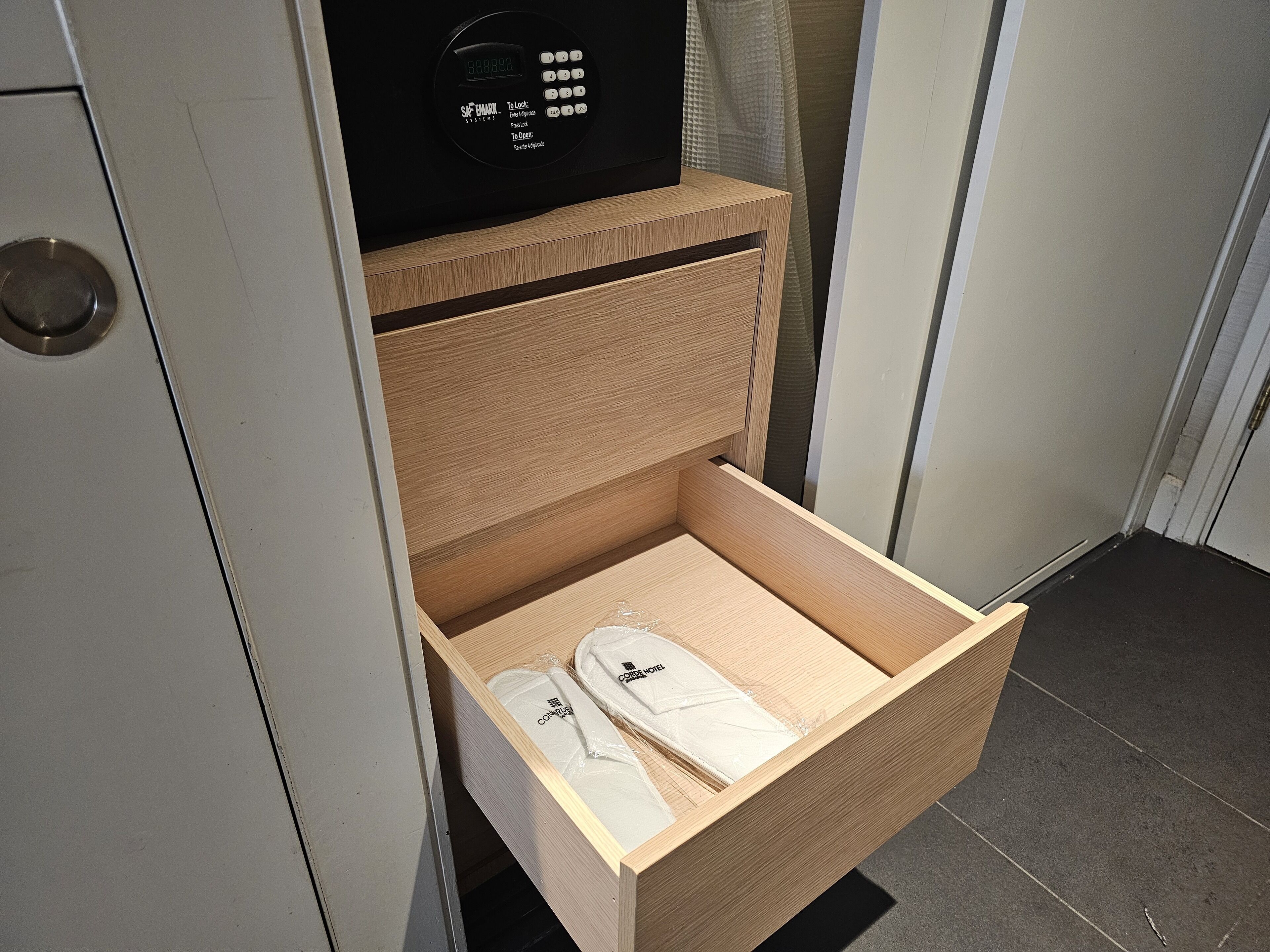 A wooden drawer with a built-in electronic device, possibly a safe or control panel, and a pair of white slippers.