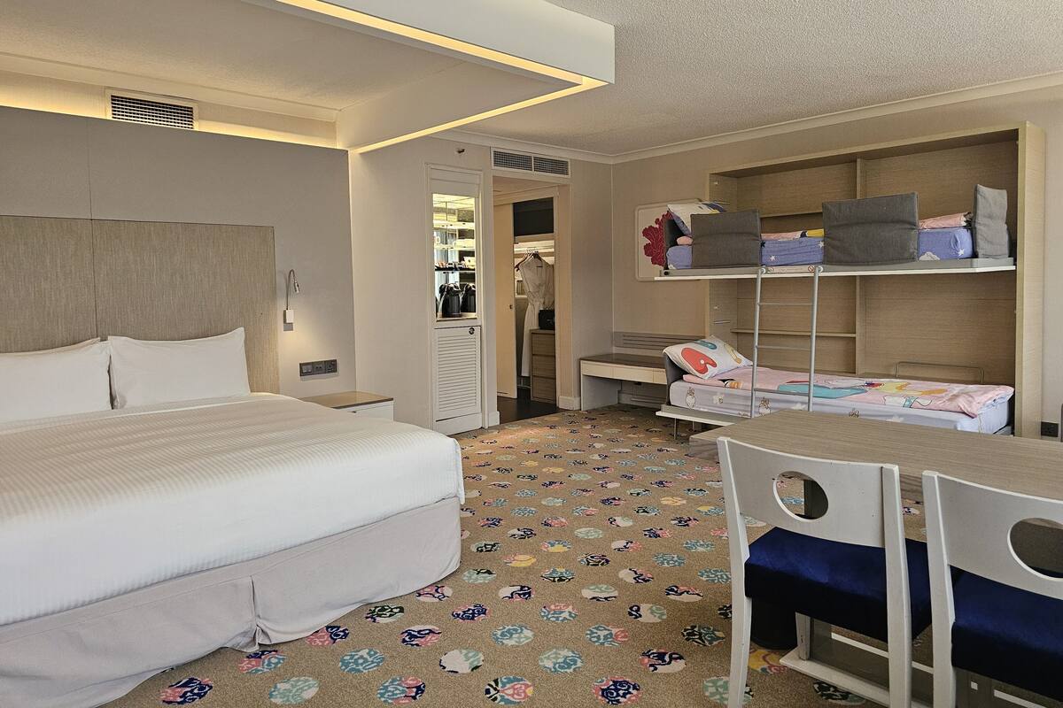 A hotel room with a bed, bedside table, desk, chair, and a wardrobe with shelves.