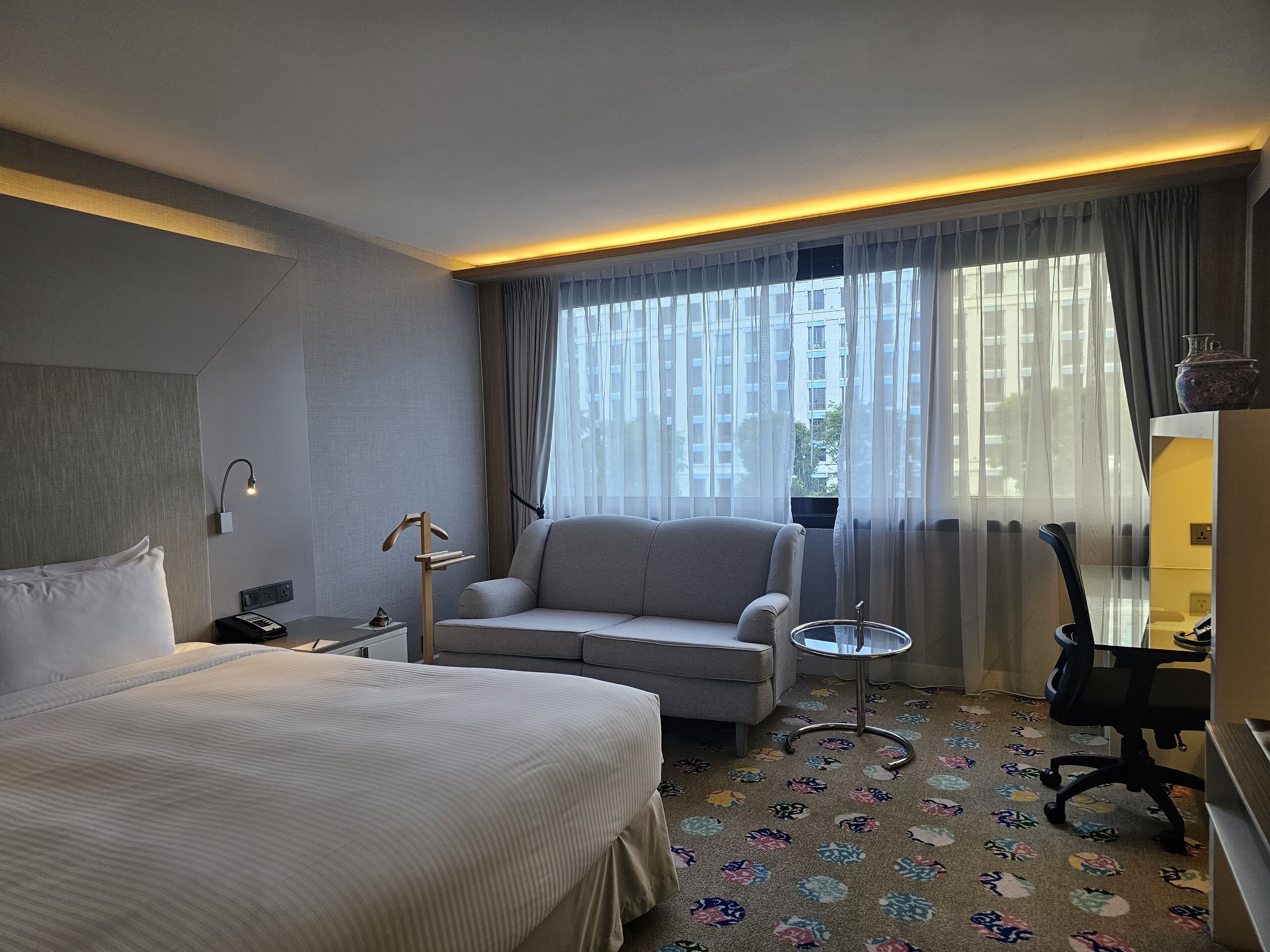 Ein Hotelzimmer mit Bett, Sofa, kleinem Tisch, Sessel und Schreibtisch.