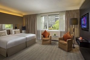 Habitación de hotel con una cama grande, dos sillones, una mesita, un televisor y una ventana con cortinas.