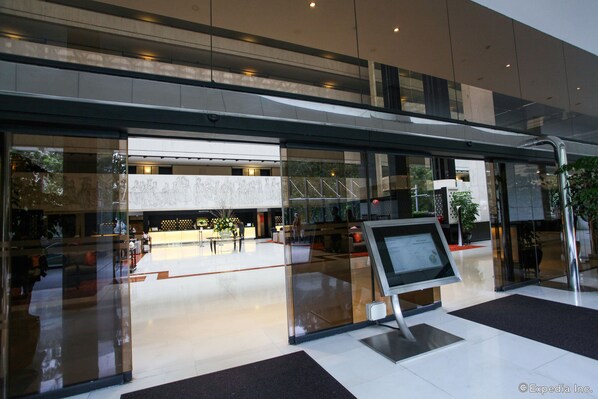 A modern hotel lobby with a reception desk, glass doors, and a digital information kiosk.