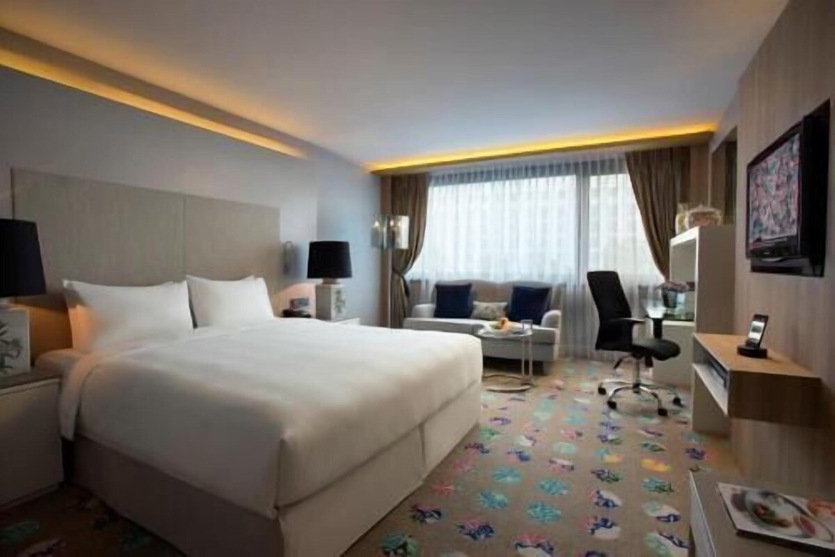 Een hotelkamer met een groot bed, een bureau met stoel, een televisie en een raam met gordijnen.