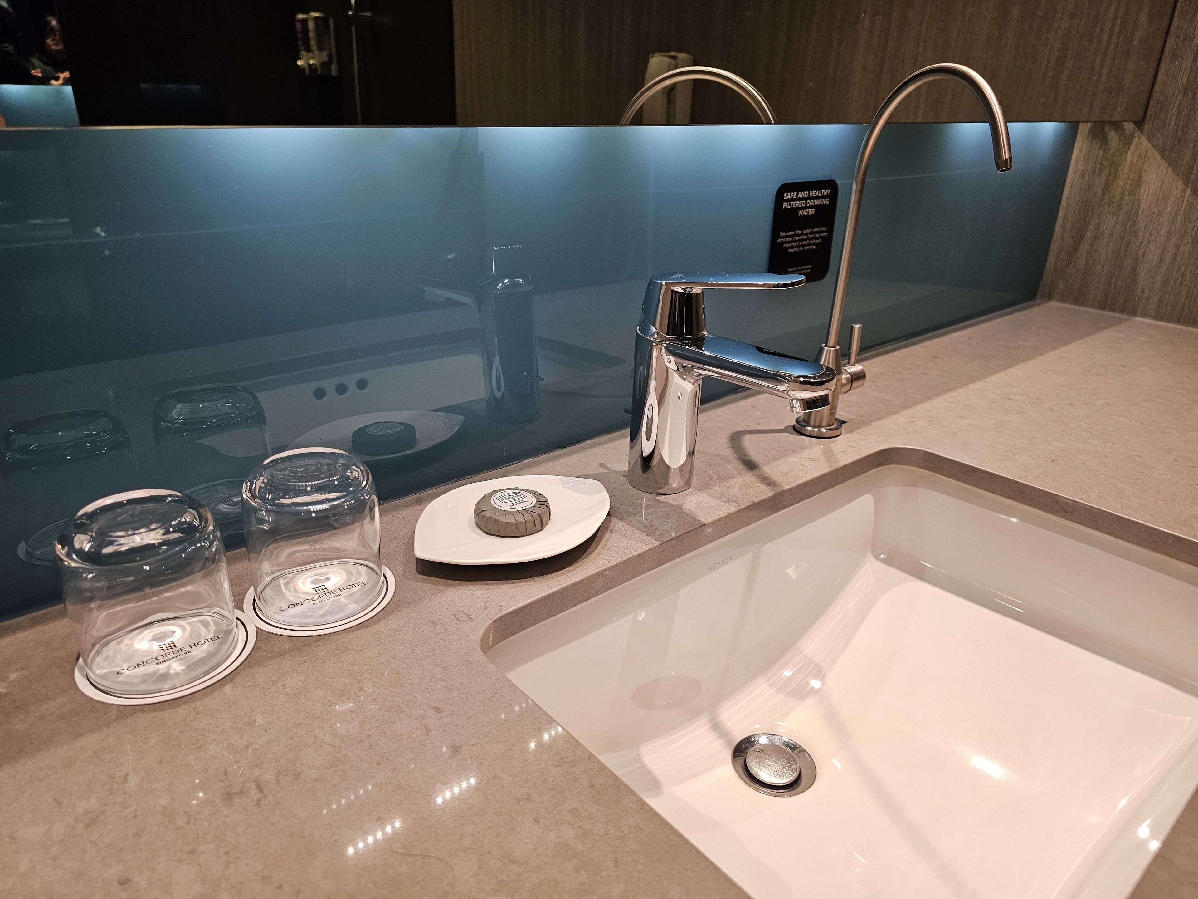 Un baño moderno con un grifo cromado, un lavabo de cristal y dos vasos transparentes sobre el mostrador.