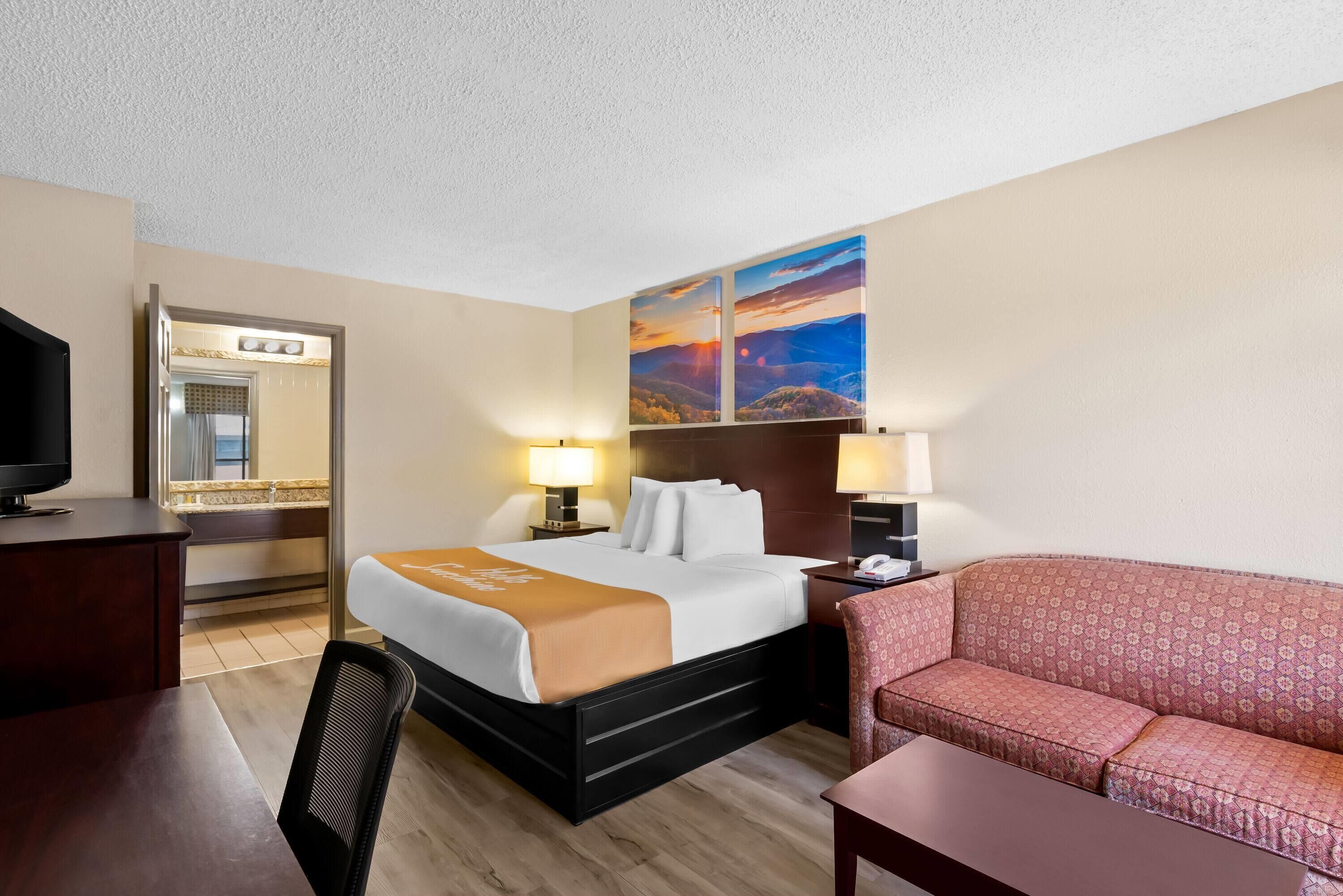A hotel room with a bed, a desk, a chair, a sofa, and a large painting on the wall.