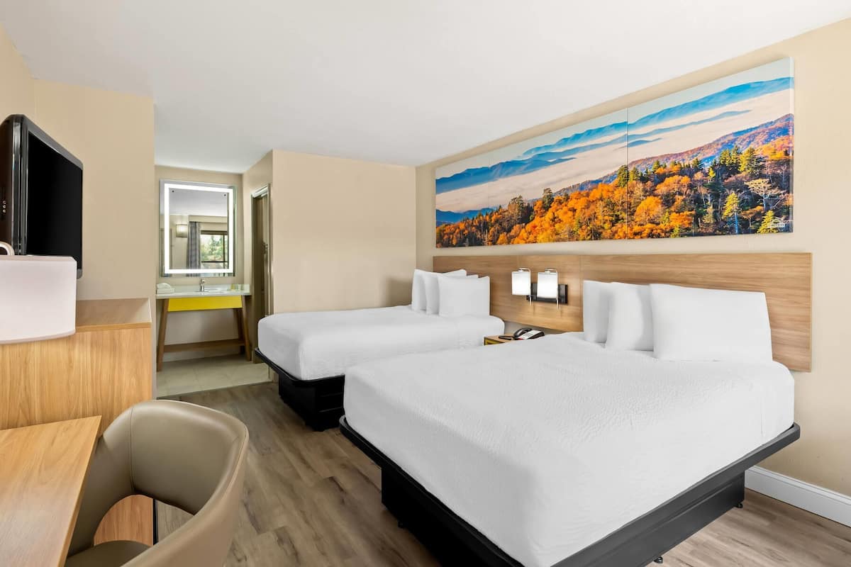 Une chambre d’hôtel avec deux lits, un bureau, une chaise, une télévision et un grand tableau au mur.