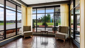 A spacious room with large windows, two armchairs, a small table, and a view of a parking lot and greenery outside. - Days Inn by Wyndham Petersburg/South Fort Lee (Petersburg)