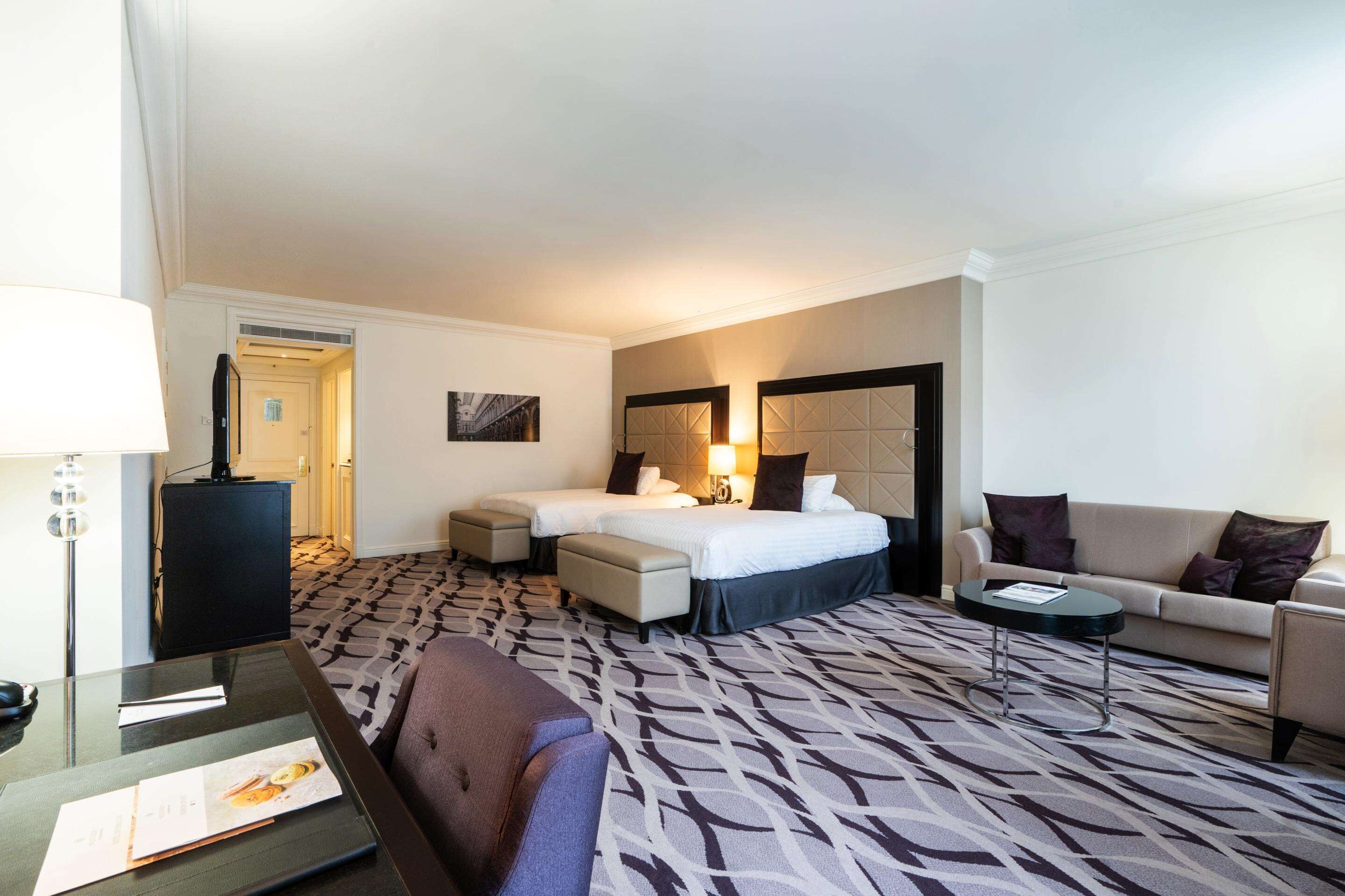 Een hotelkamer met twee bedden, een bank, een salontafel en een bureau met lamp.