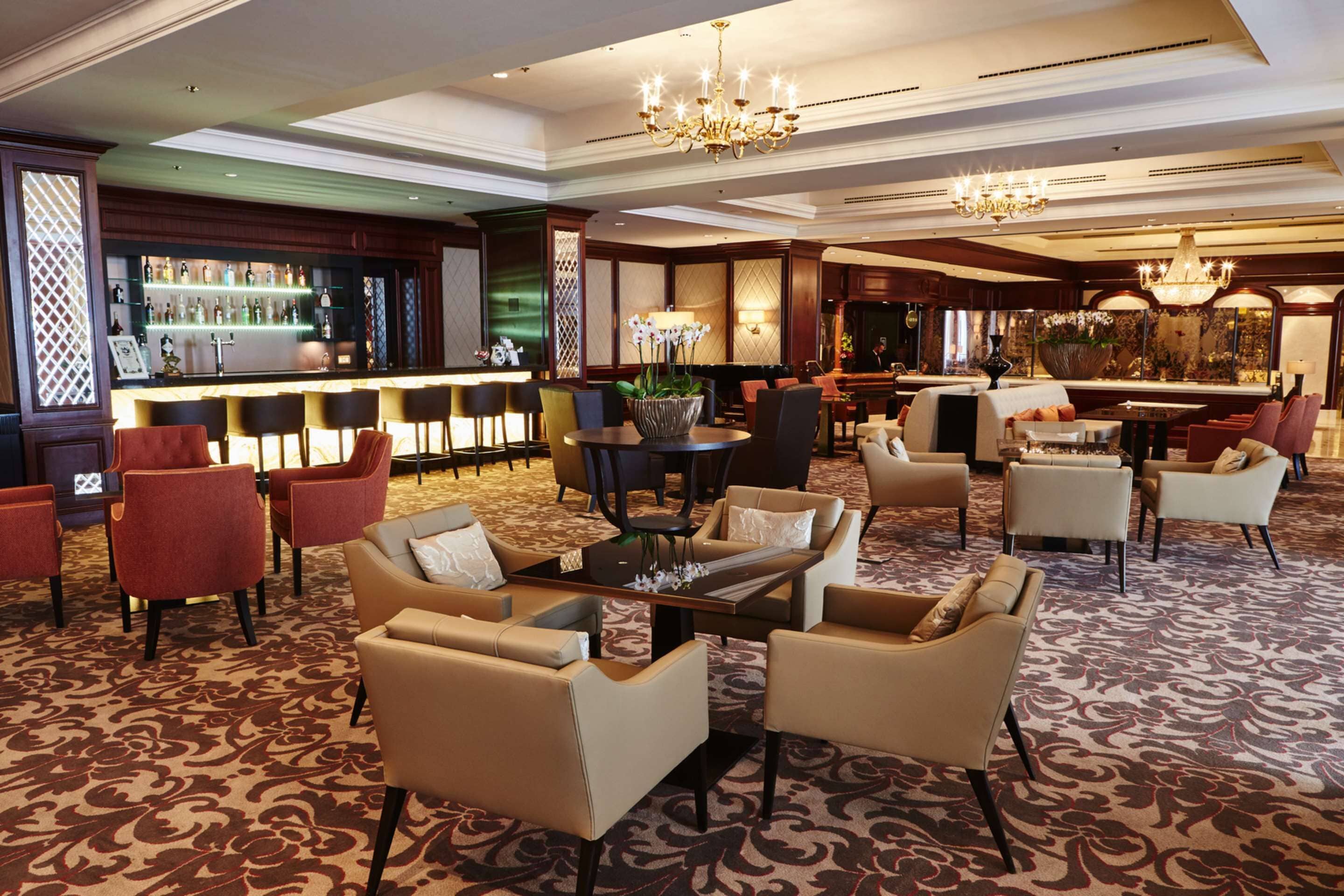 A spacious lobby with a bar area, multiple seating arrangements, and decorative lighting fixtures.