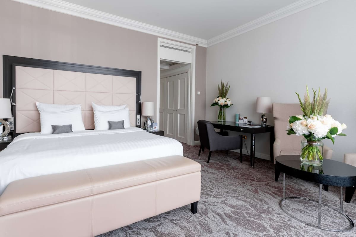 A hotel room with a large bed, a desk, a chair, and a small table.