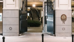 Una entrada imponente con fachada blanca, una gran letra 'W' ornamentada sobre las puertas y una escalera que conduce a un nivel superior.